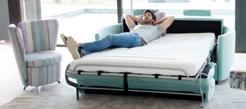 A man relaxing on an amazing green fama sofa bed.