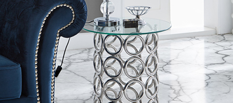 Silver round side table with glass top near a blue sofa in a living room.