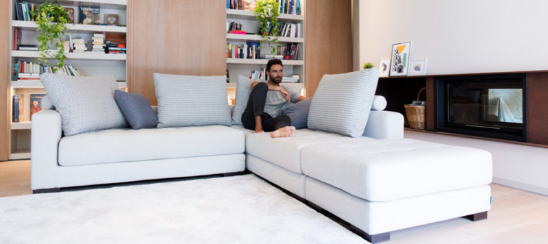 Fama corner sofa in grey colour with a guy relaxing on it in his living room.