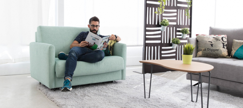 Man reading on a comfy green sofa made in spain.